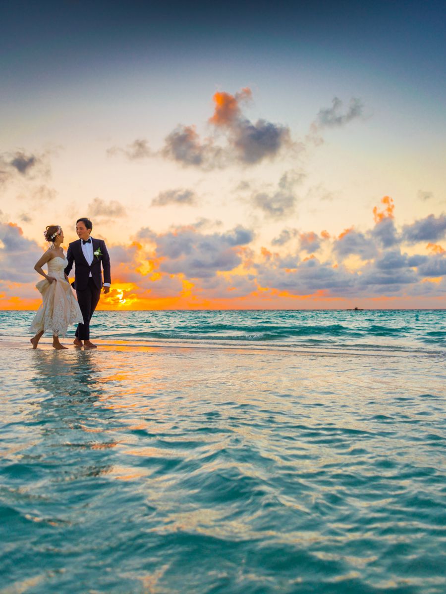 Bride and groom walking through the surf at sunset under an orange sky