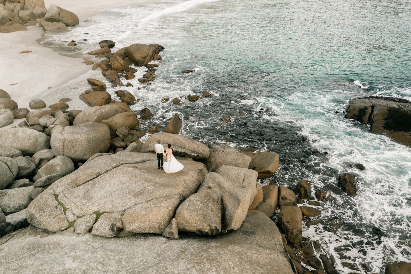 Aerial view of a couple standing on rocks above green water