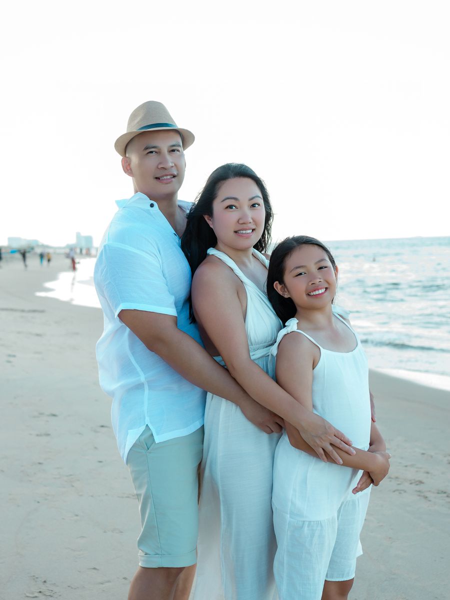 Family of three in white and light blue on the beach