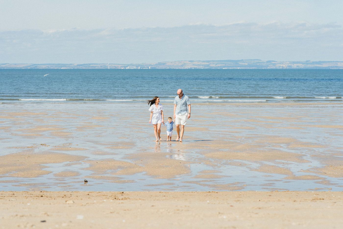 Parents and a small child walking along wet sand at low tide