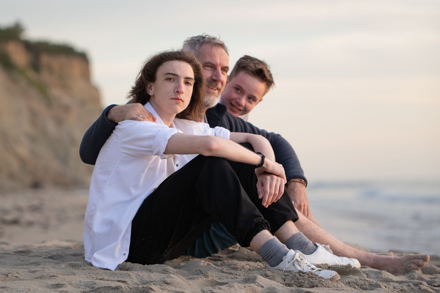 Three family members sitting close together on the sand