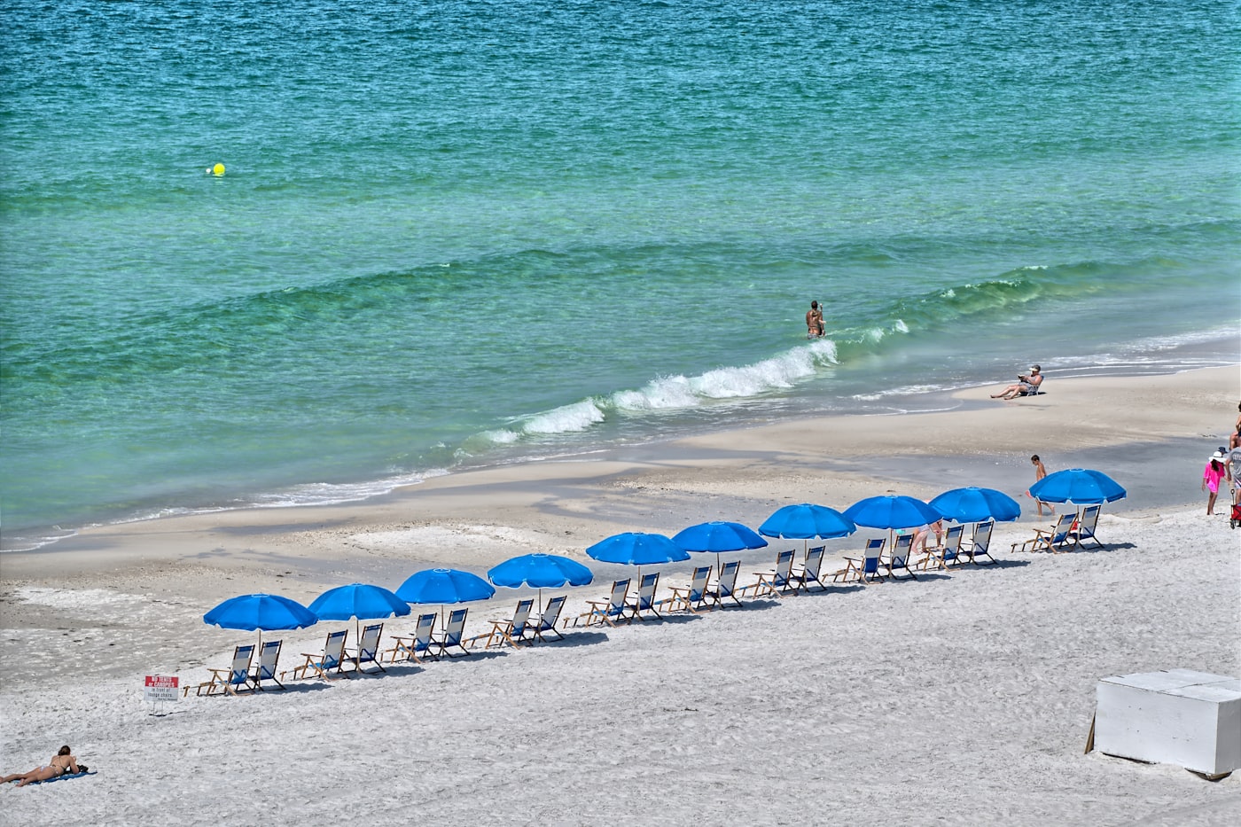 A row of blue umbrellas on white sand beside bright green Gulf water