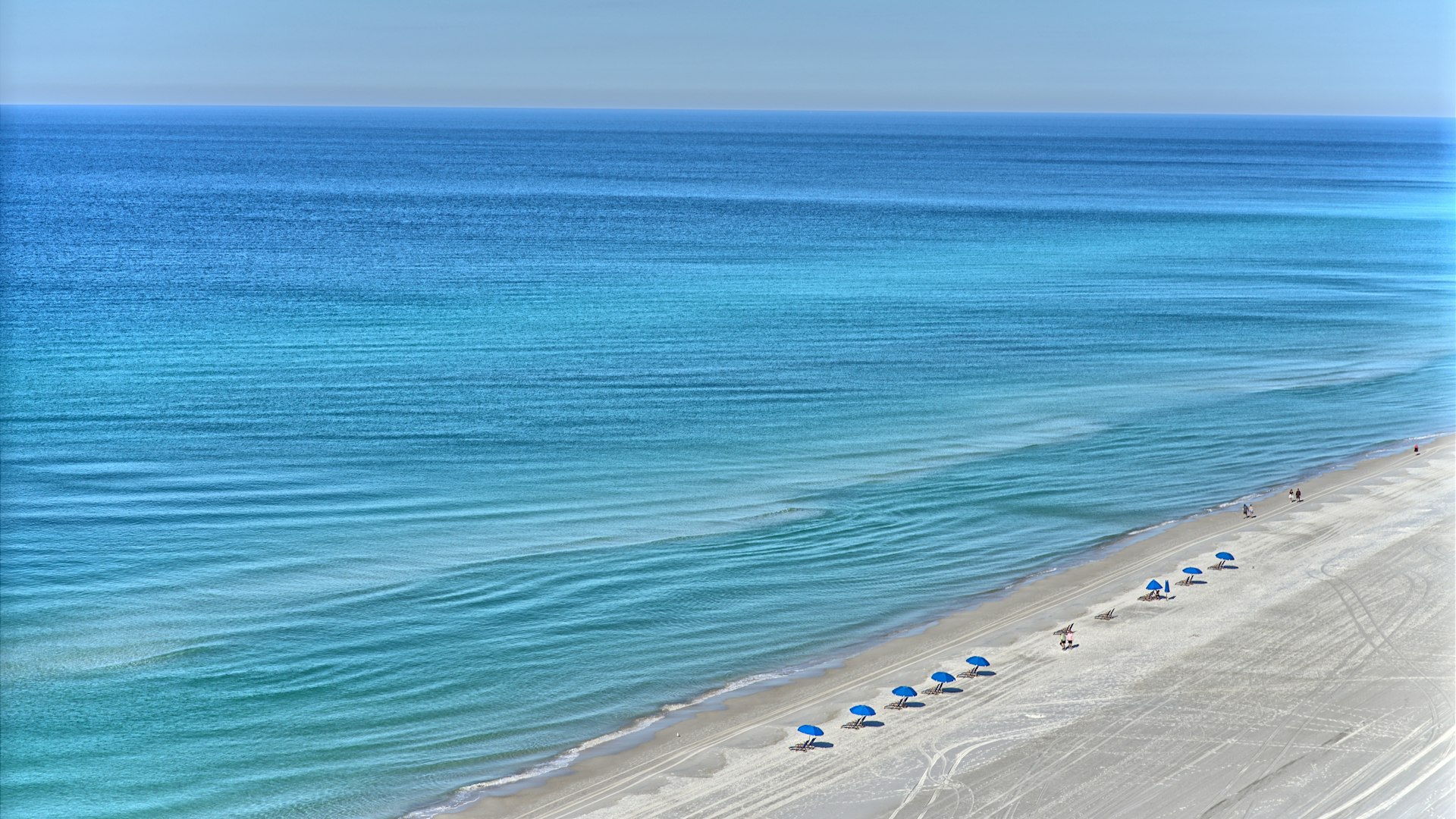 Aerial view of turquoise water meeting a white-sand beach lined with umbrellas