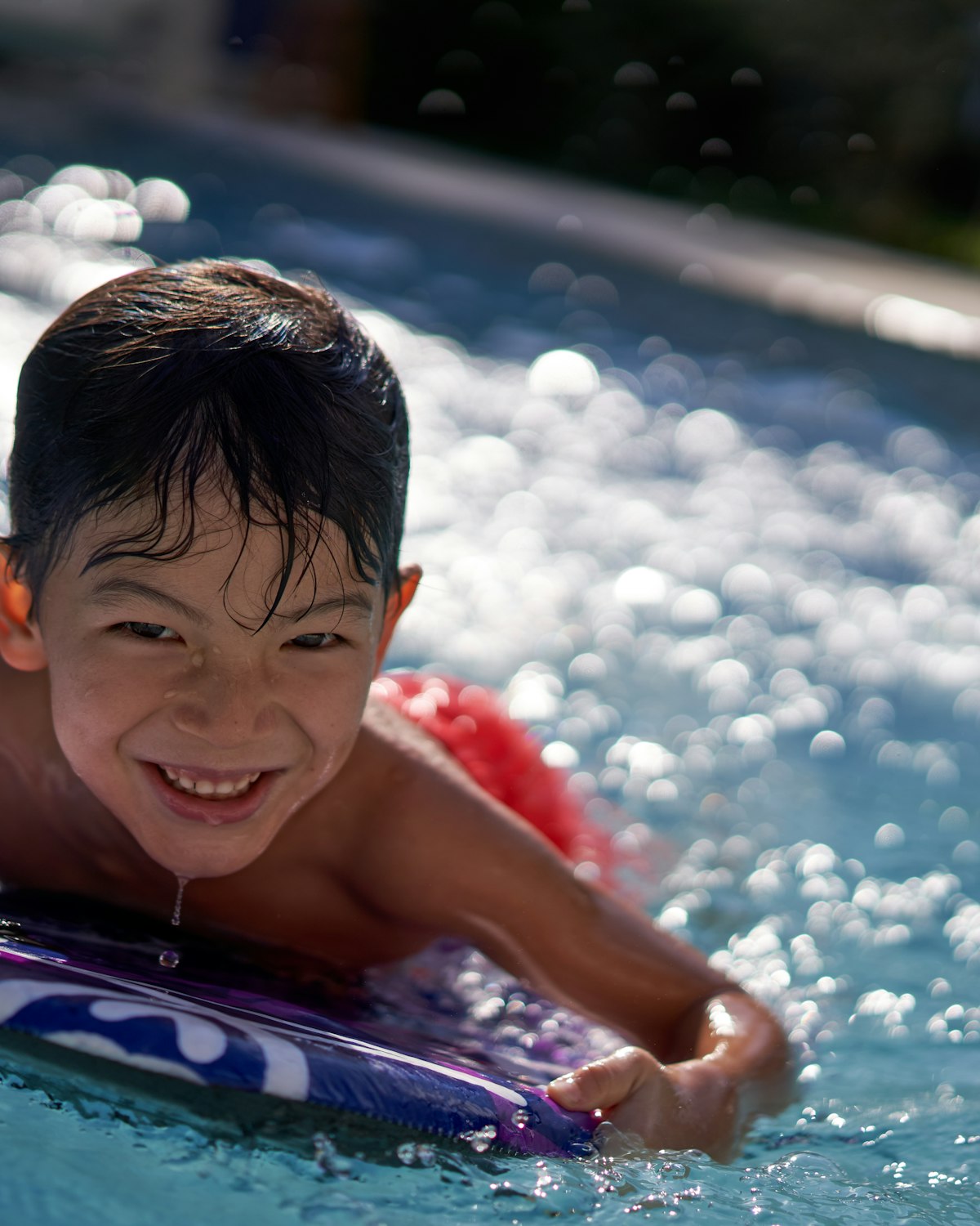 A smiling boy in the water, hair wet, mid-splash