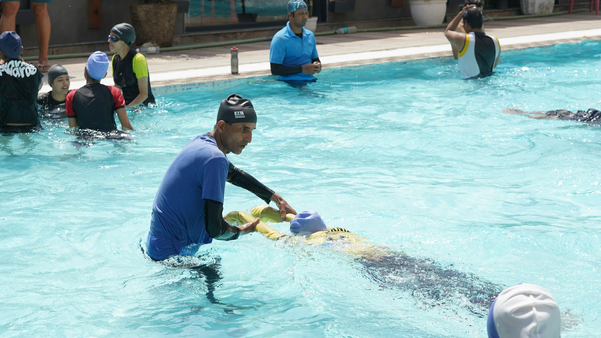 A swim instructor in the pool guiding a young child on a kickboard