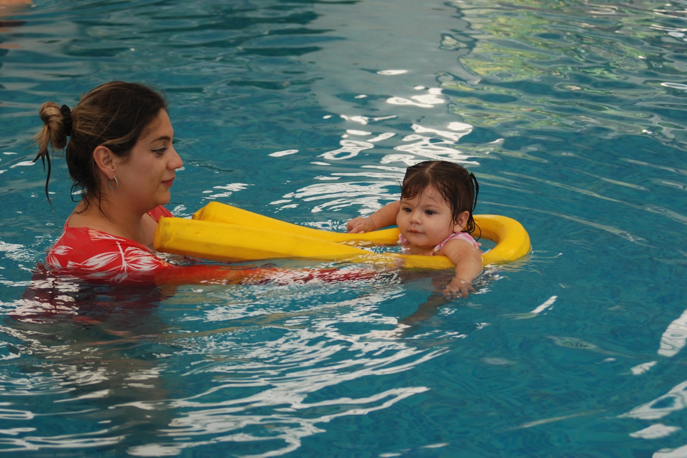 A parent in the pool holding a toddler on a yellow float